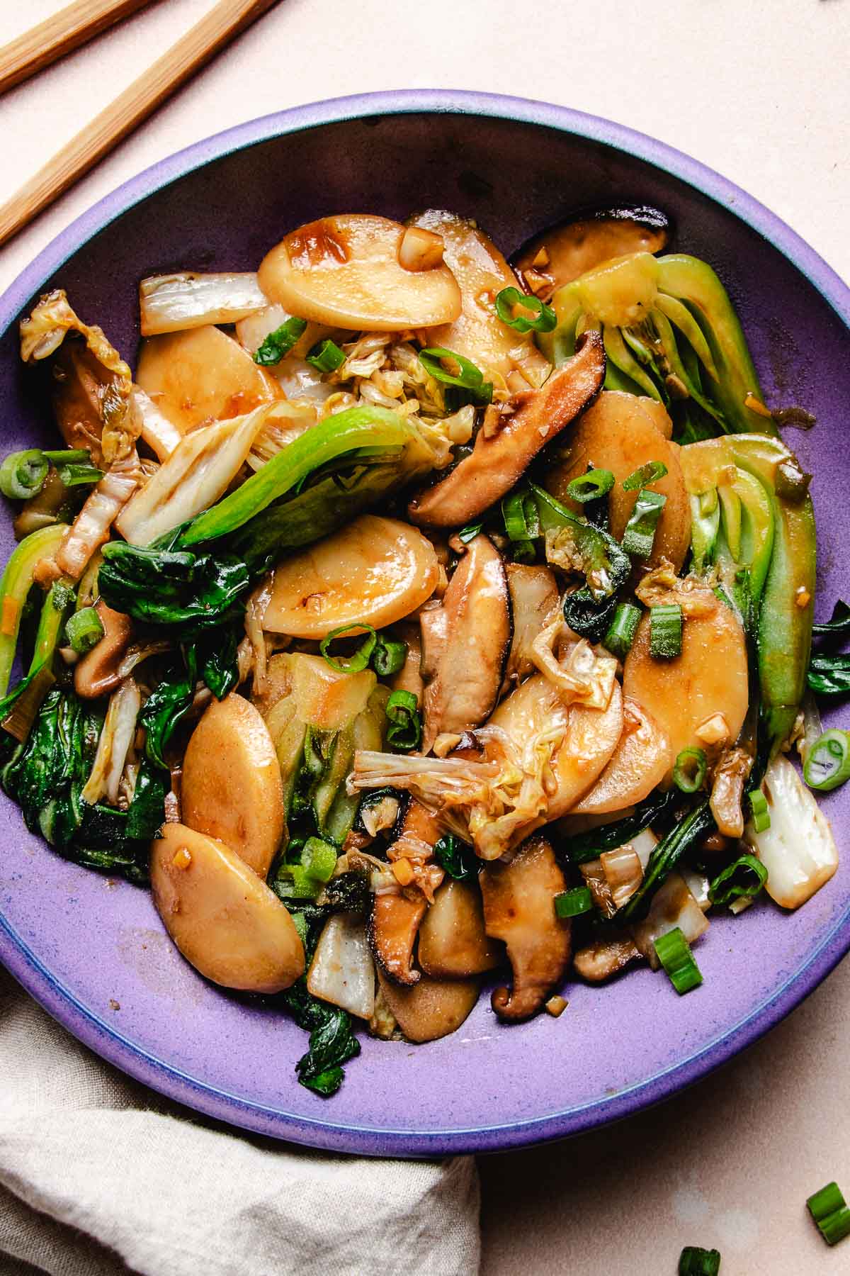 Image shows stir fried Shanghai rice cake with napa cabbage and bok choy in Asian brown sauce on a purple color plate.
