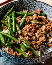 Feature image shows ground chicken and green beans stir fried and served in a blue color bowl with steamed rice.
