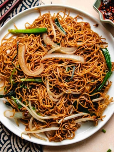 Feature image shows crispy Cantonese chow mein noodles with bean sprouts, onion, and garlic give served in a big white plate.