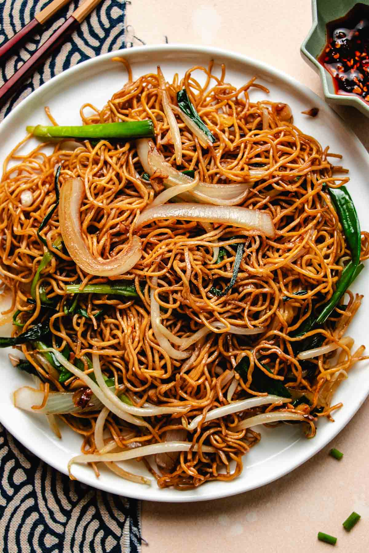 Feature image shows crispy Cantonese chow mein noodles with bean sprouts, onion, and garlic give served in a big white plate.