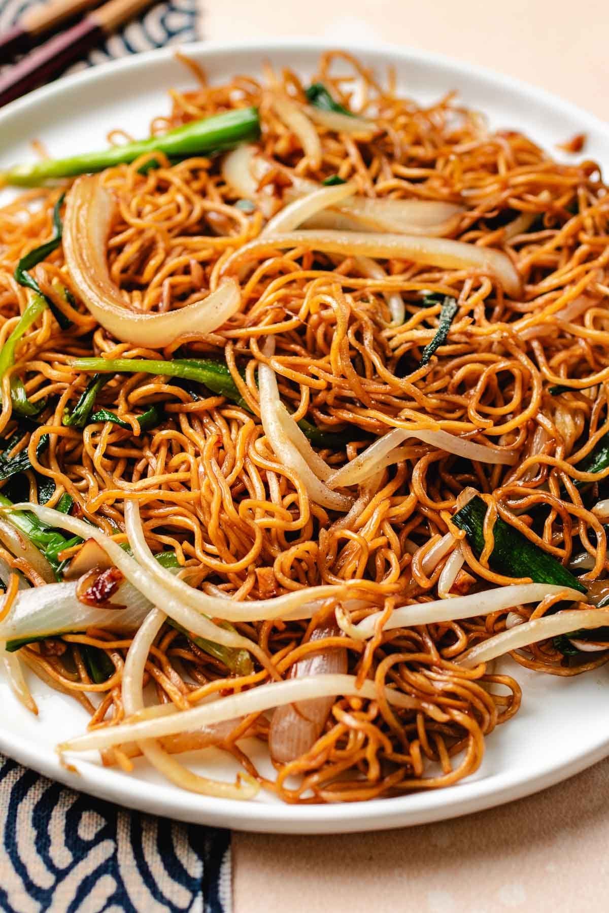 A side close shot show cases the crispy texture of the chow mein with fresh bean sprouts and vegetables served on a white plate.
