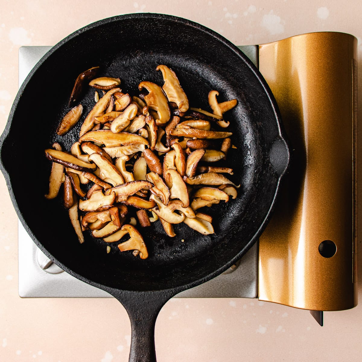Photo shows sliced shiitake mushrooms saute in a cast iron pan.