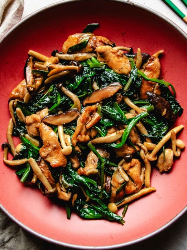 Image shows chicken breast stir fried with oyster sauce with shiitake and snow pea leaves in a red color plate.