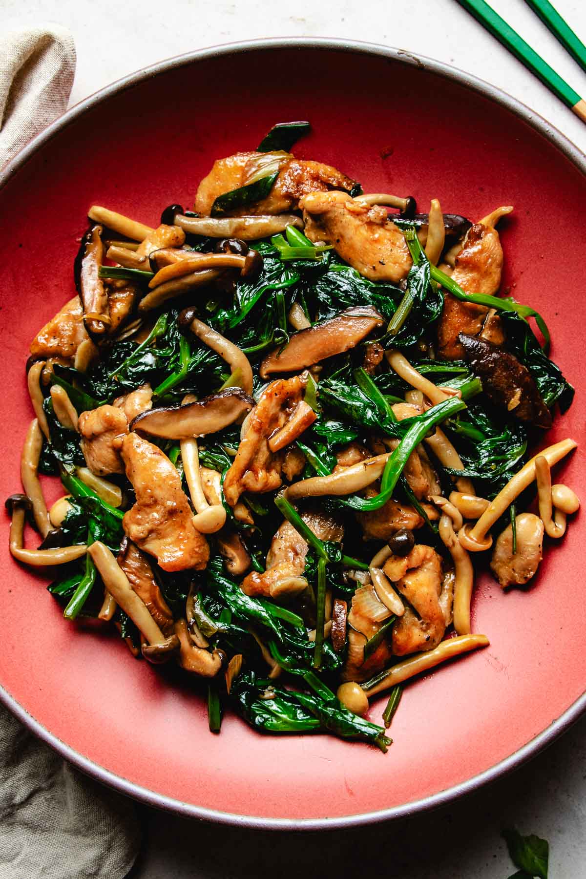 Image shows chicken breast stir fried with oyster sauce with shiitake and snow pea leaves in a red color plate.