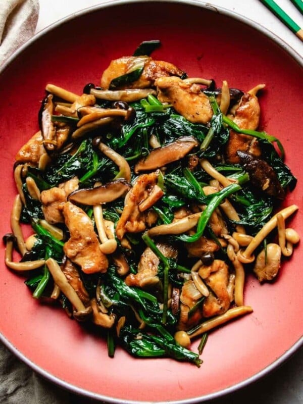 Image shows chicken breast stir fried with oyster sauce with shiitake and snow pea leaves in a red color plate.