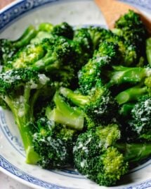 Feature image shows garlic broccoli that is tender and coated with garlic sauce and served in a blue white color plate.