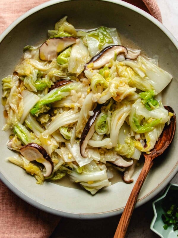 Image shows sauteed napa cabbage with garlic ginger and shiitake mushrooms Asian style served in a light gray color plate.