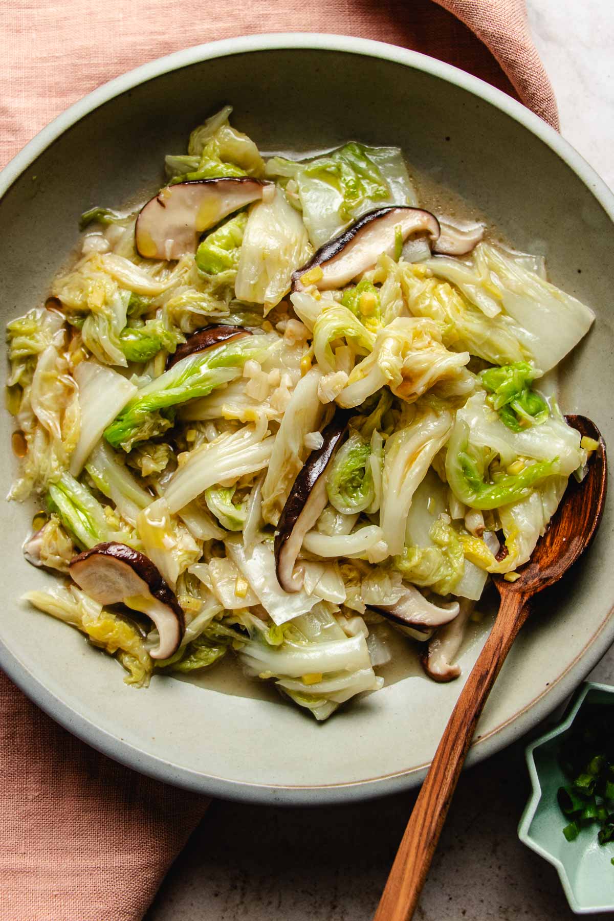 Image shows sauteed napa cabbage with garlic ginger and shiitake mushrooms Asian style served in a light gray color plate.