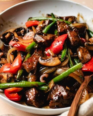 A side shot shows Panda Express black pepper angus steak dish with tender beef cubes and crispy veggies made gluten-free in a white serving plate.