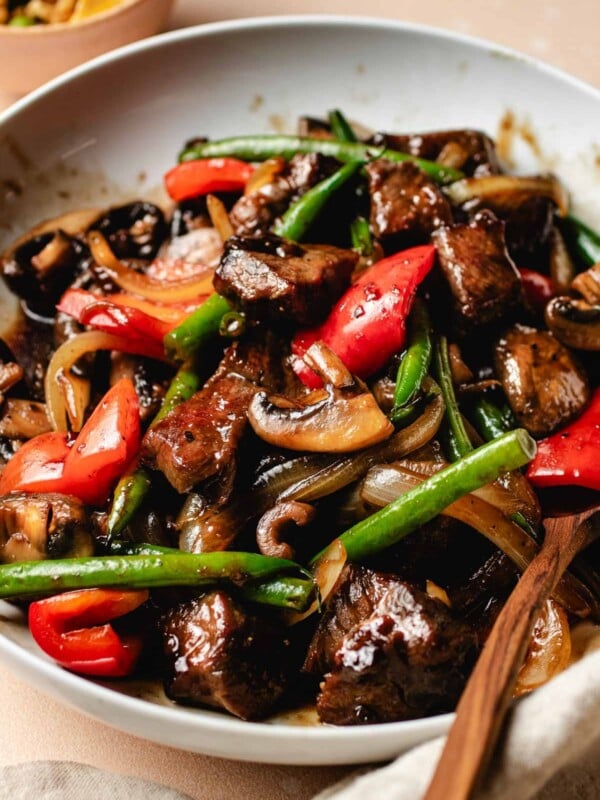 A side shot shows Panda Express black pepper angus steak dish with tender beef cubes and crispy veggies made gluten-free in a white serving plate.