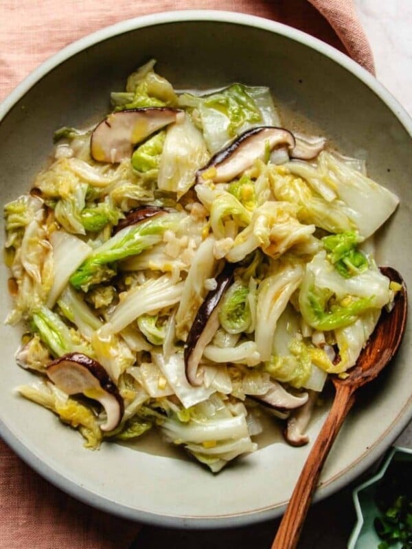 Image shows sauteed napa cabbage with garlic ginger and shiitake mushrooms Asian style served in a light gray color plate.