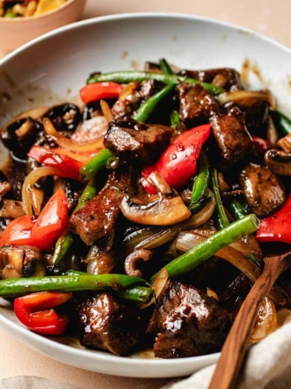 A side shot shows Panda Express black pepper angus steak dish with tender beef cubes and crispy veggies made gluten-free in a white serving plate.