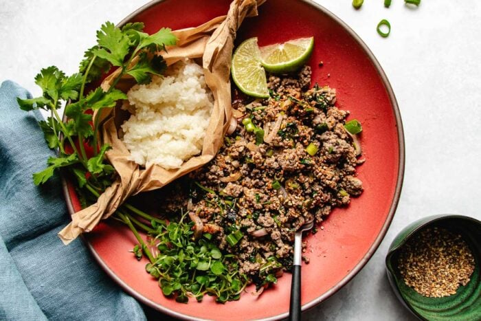 Feature image shows Thai beef laab served with sticky rice and toasted rice powder on the side.