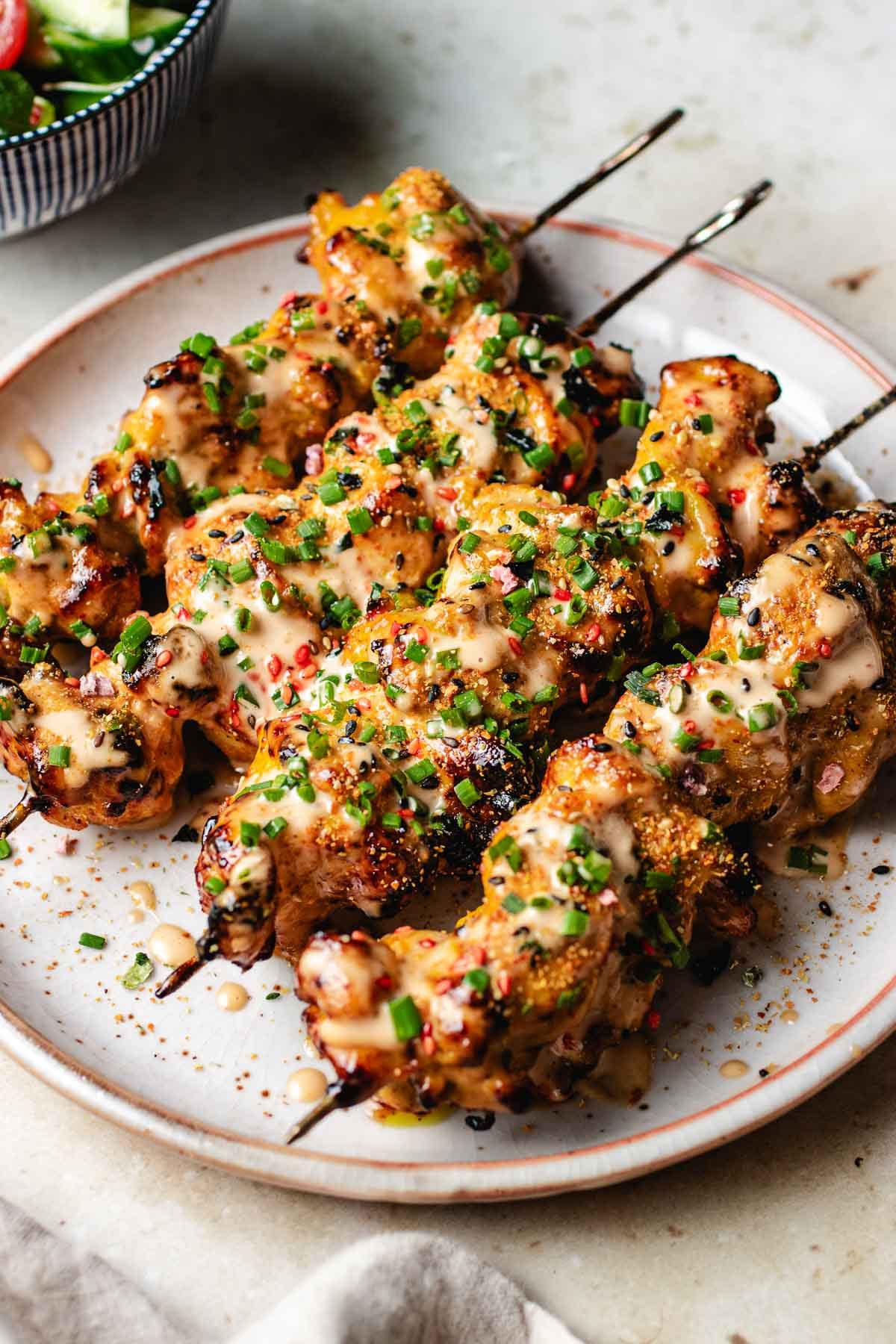 A side close shot shows bang bang chicken skewers brushed with sauce and garnish on top.