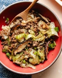 A close overhead shot shows ground beef stir fried to perfectly browned with cabbage and shiitake and served with rice in a red bowl.