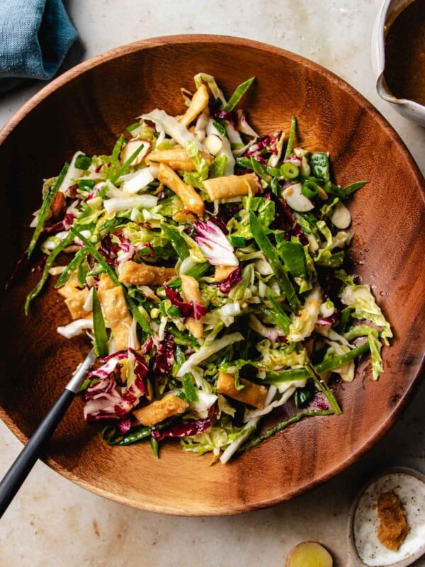 Feature image shows napa cabbage slaw served in a wood plate and tossed with dressing.