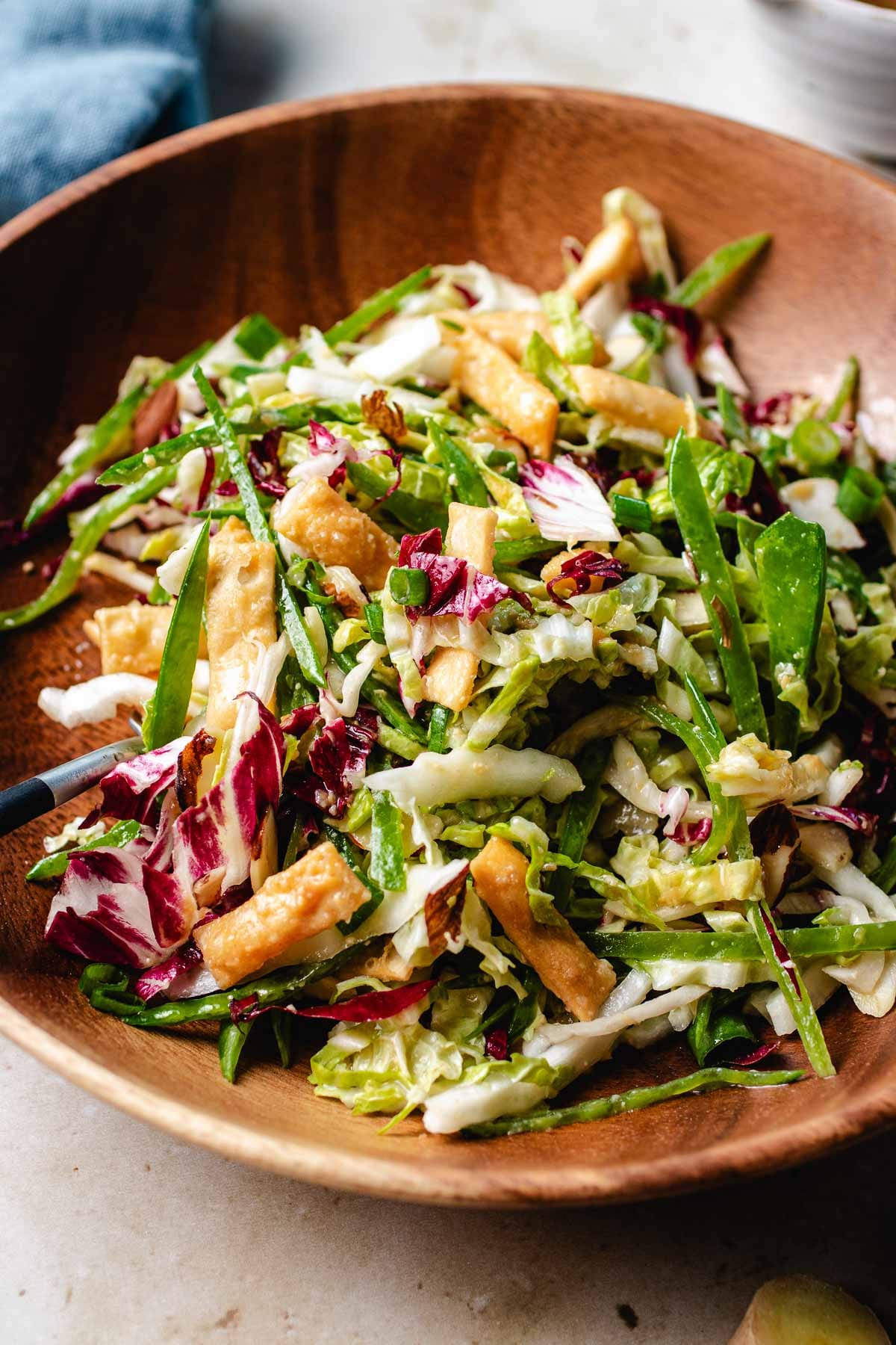 A side close shot image shows napa slaw served in a wood plate and tossed with dressing.