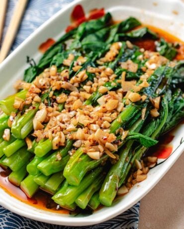 A close shot shows blanched yu choy stacked onto a serving plate and covered with minced garlic with garlic sauce.