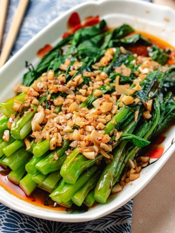 A close shot shows blanched yu choy stacked onto a serving plate and covered with minced garlic with garlic sauce.