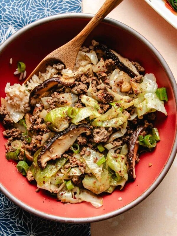 A close overhead shot shows ground beef stir fried to perfectly browned with cabbage and shiitake and served with rice in a red bowl.