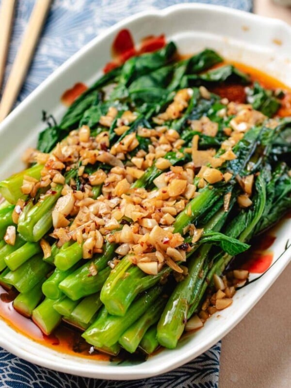 A close shot shows blanched yu choy stacked onto a serving plate and covered with minced garlic with garlic sauce.