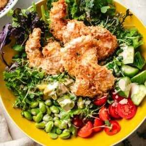 An overhead image shows crunchy bang bang shrimp served with a bowl of colorful fresh greens and vegetables in a yellow bowl.