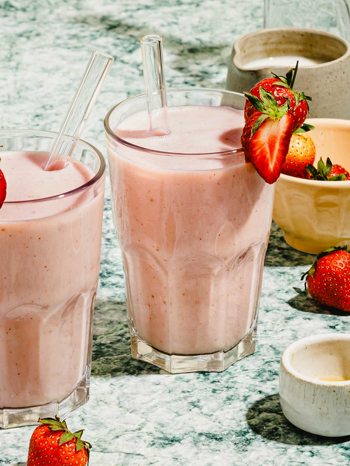 Image shows two glasses of strawberry almond milk serve chilled with strawberries on top.