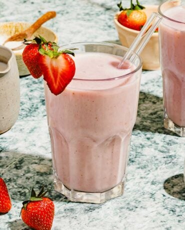 Image shows a glass of strawberry almond milk blended to creamy frothy, garnish with strawberry on top in a glass.