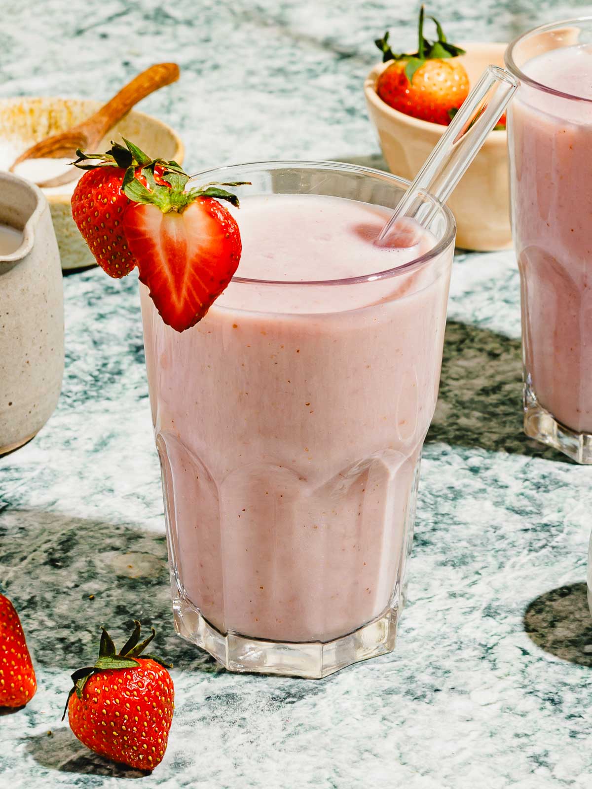 Image shows a glass of strawberry almond milk blended to creamy frothy, garnish with strawberry on top in a glass.