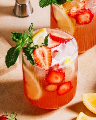 Feature image shows 2 glasses of Strawberry lemonade vodka served with fresh strawberry, lemon and mint leaves.