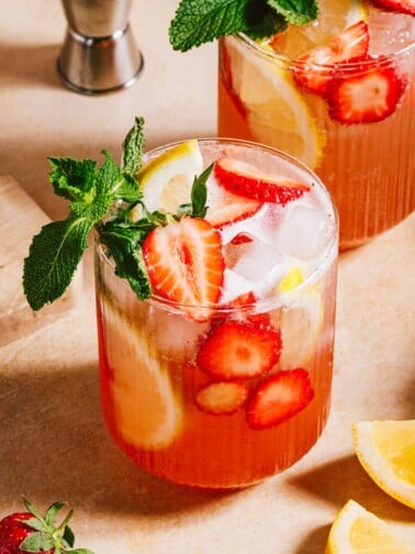 Feature image shows 2 glasses of Strawberry lemonade vodka served with fresh strawberry, lemon and mint leaves.