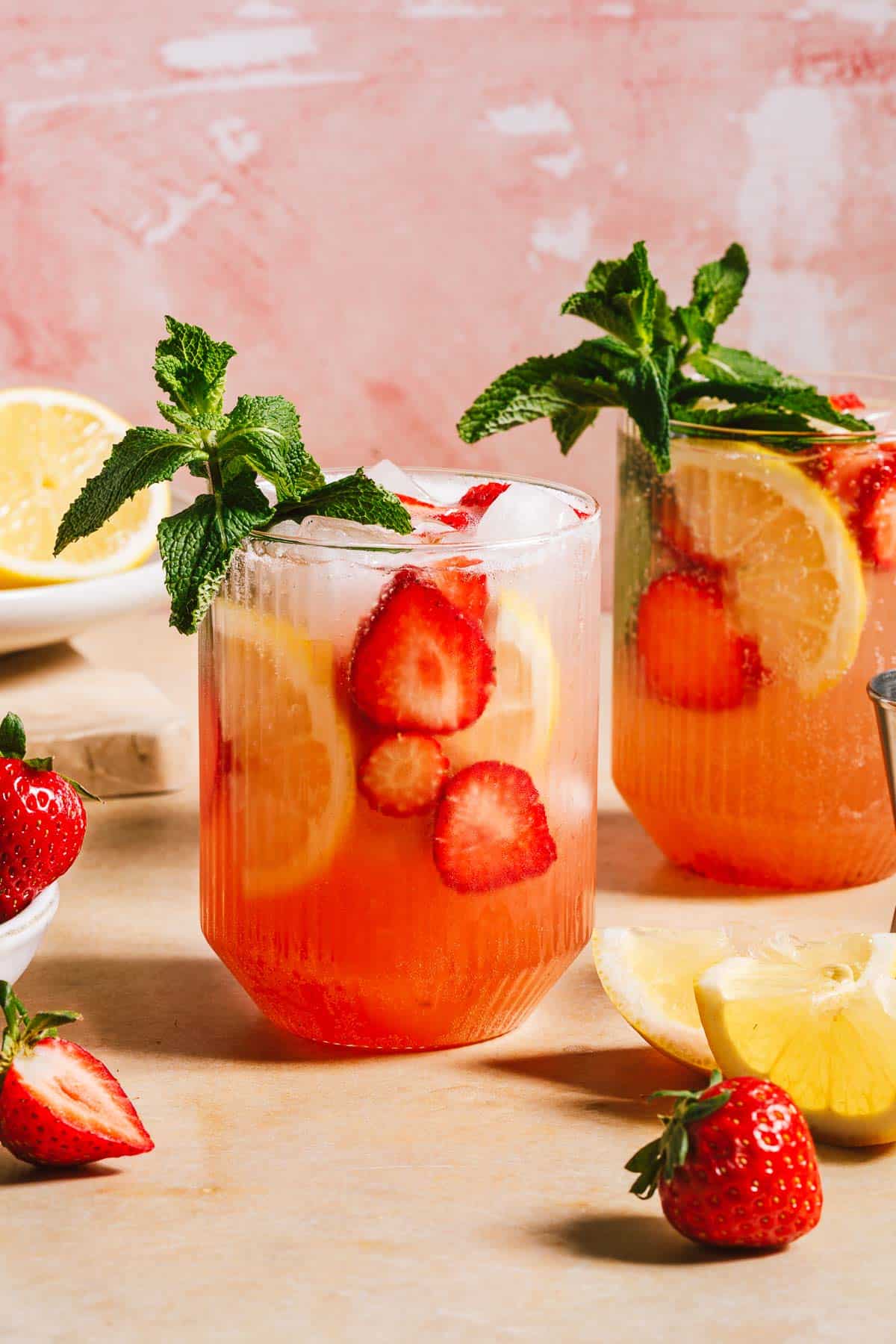A hero shot image shows 2 glasses of strawberry vodka cocktails with slices of strawberries and lemon in the glass with sparking water,