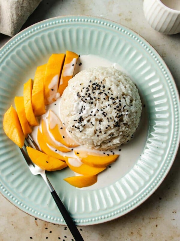 Feature image shows coconut sticky rice with mango served on a light blue color plate with sticky rice sauce.