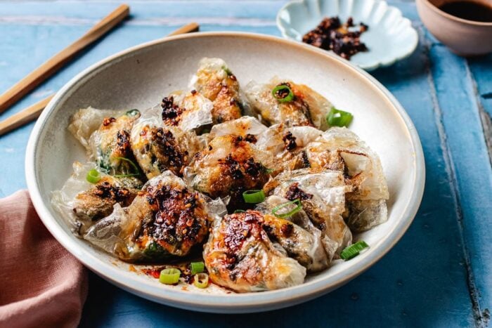 Image shows a plate of crispy rice paper garlic chive dumplings drizzled with dumpling sauce.