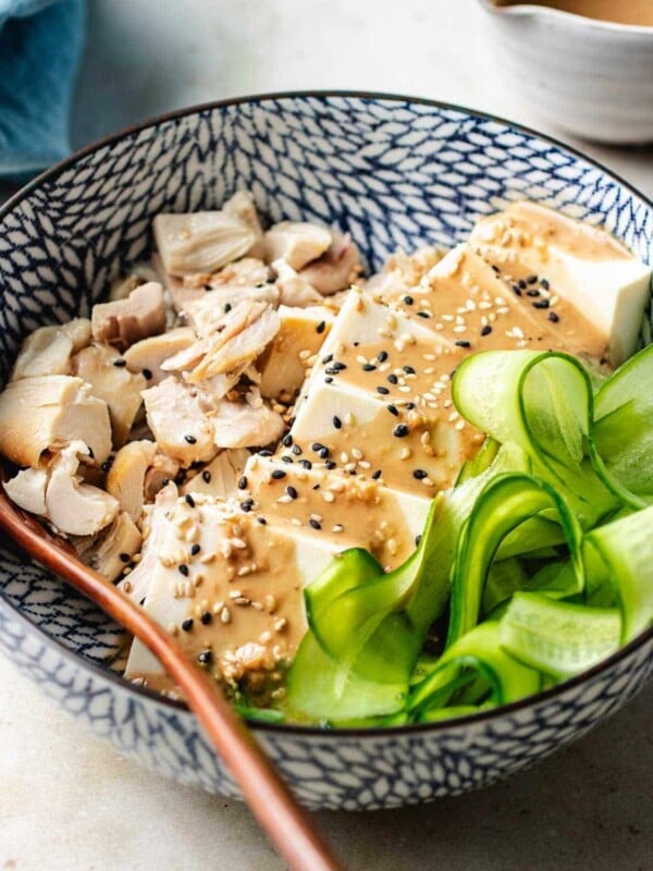 Photo shows a bowl of silken cold tofu salad bowl with garlic sesame tofu dressing served with cucumber and chicken.