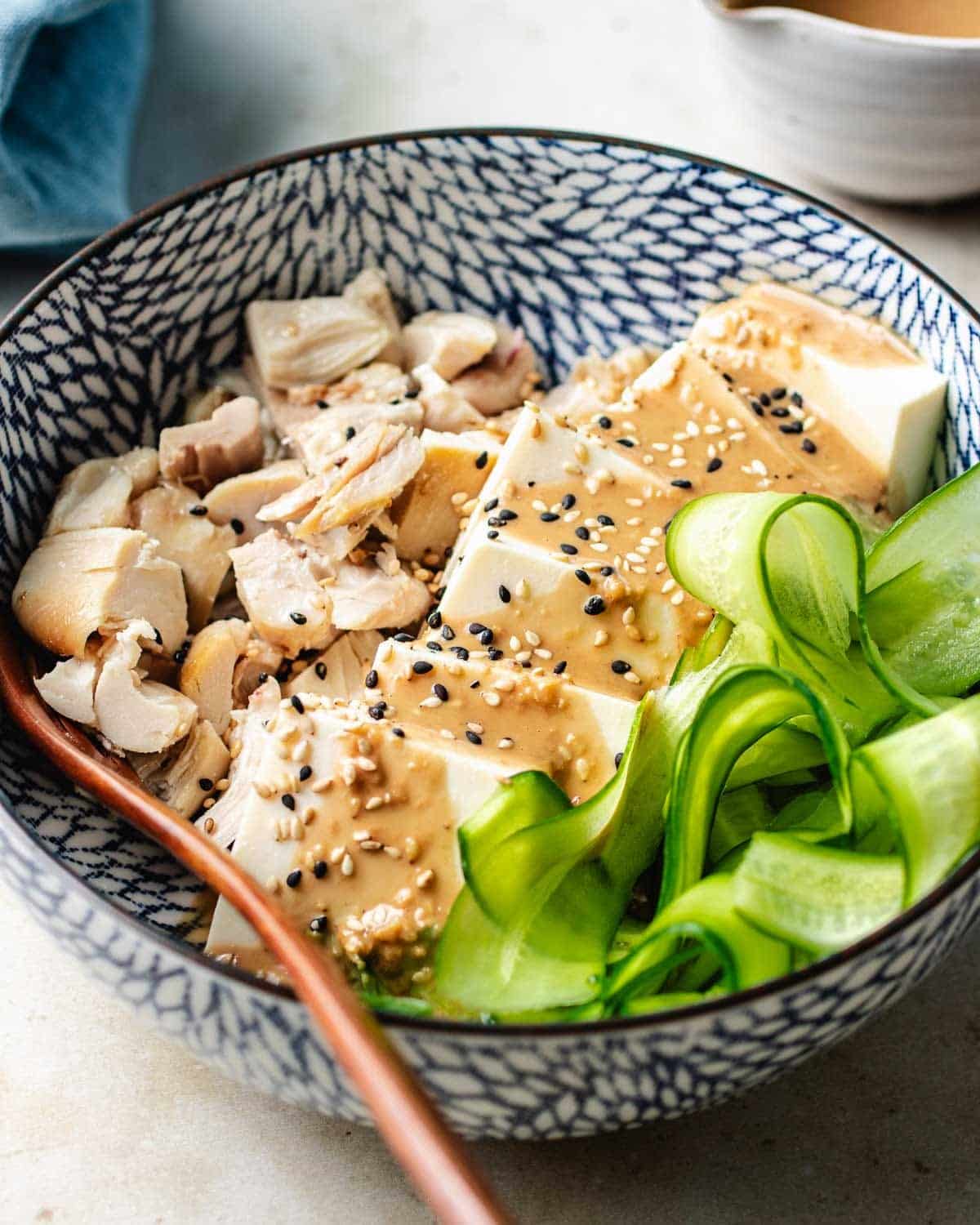 Photo shows a bowl of silken cold tofu salad bowl with garlic sesame tofu dressing served with cucumber and chicken.