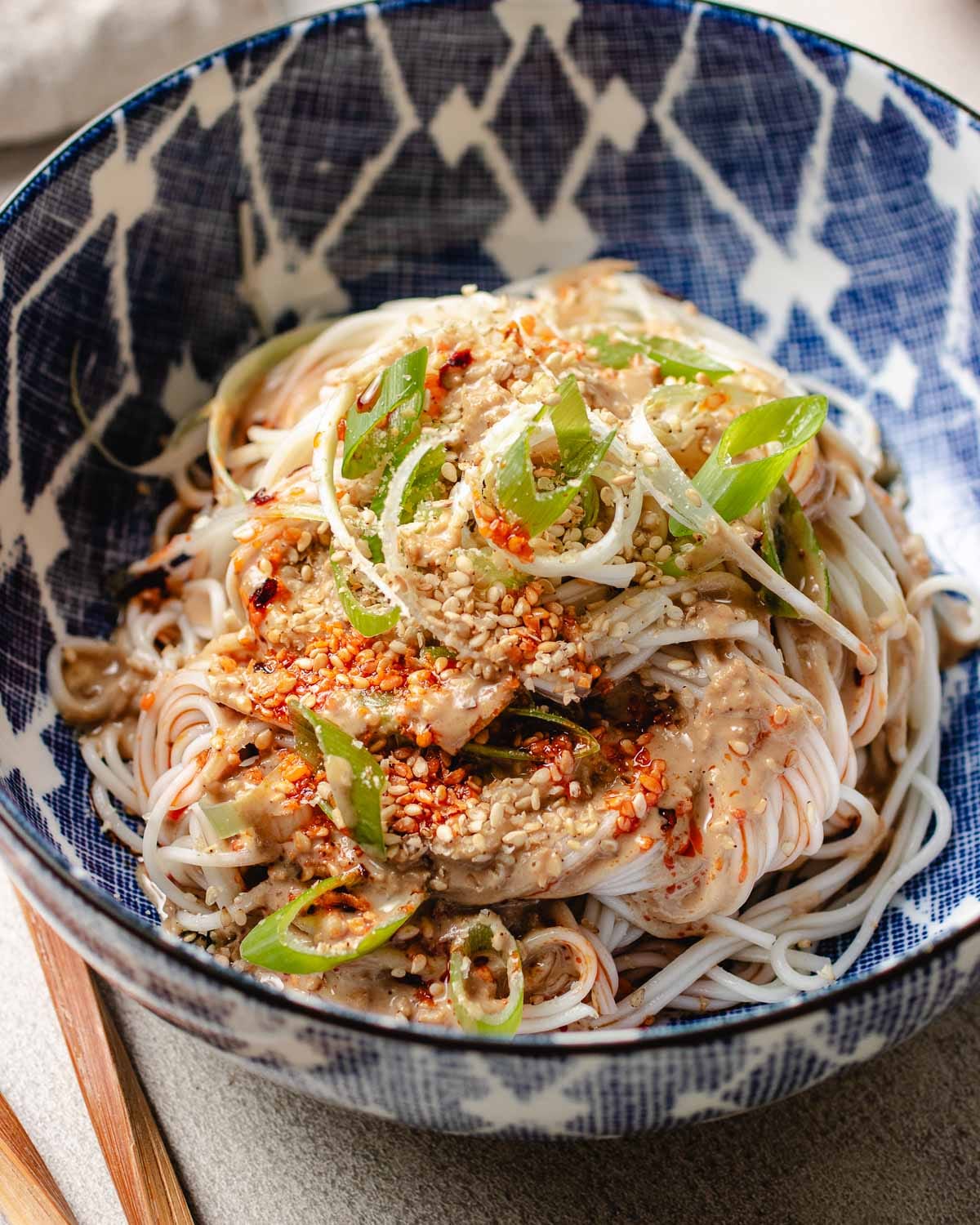 A close shot shows cold noodles drizzled with sesame sauce and chili oil, served in a bowl.