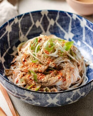 Feature image shows a bowl of cold noodles covered in Taiwanese sesame sauce served in a blue white color bowl with sesame seeds on top.