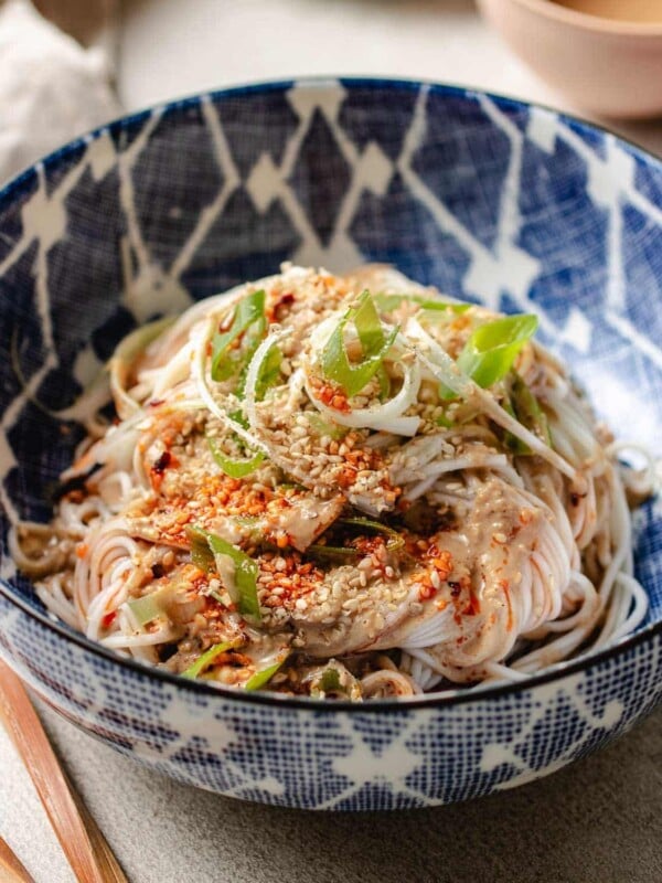 Feature image shows a bowl of cold noodles covered in Taiwanese sesame sauce served in a blue white color bowl with sesame seeds on top.