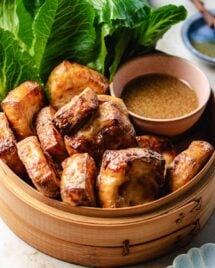 Feature image shows tofu puffs with golden brown color outside and fluffy inside, served in a bamboo basket with dipping sauce and lettuce greens on the side.