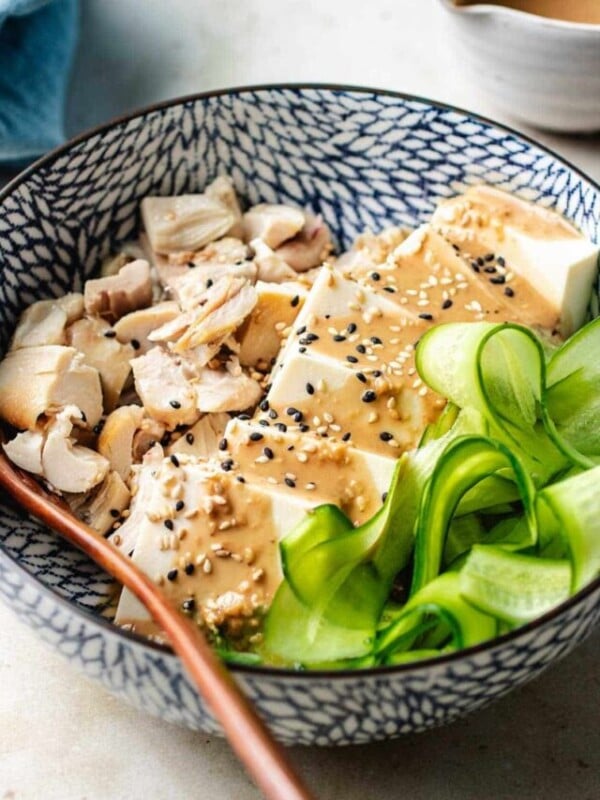 Photo shows a bowl of silken cold tofu salad bowl with garlic sesame tofu dressing served with cucumber and chicken.