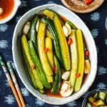 Recipe image shows Asian pickled cucumbers sliced into spears with soy pickling marinade with chili peppers on top.