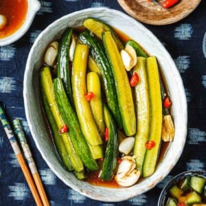 Recipe image shows Asian pickled cucumbers sliced into spears with soy pickling marinade with chili peppers on top.