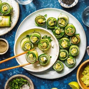 Feature image shows cucumber roll ups with avocado and turkey deli meat, served on a white plate with chopsticks.