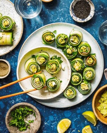 Feature image shows cucumber roll ups with avocado and turkey deli meat, served on a white plate with chopsticks.