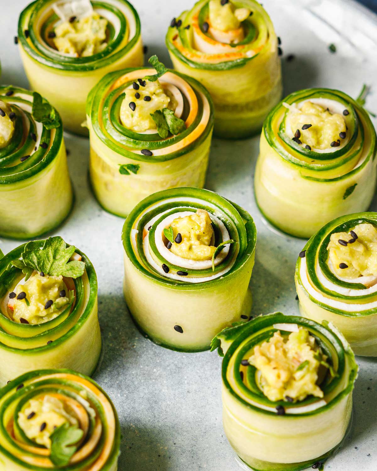 A side close shot shows individually rolled cucumber bites served on a white plate.