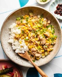 An overhead image shows a plate of sweet corn kernels sauteed with chicken and served with rice on a plate.
