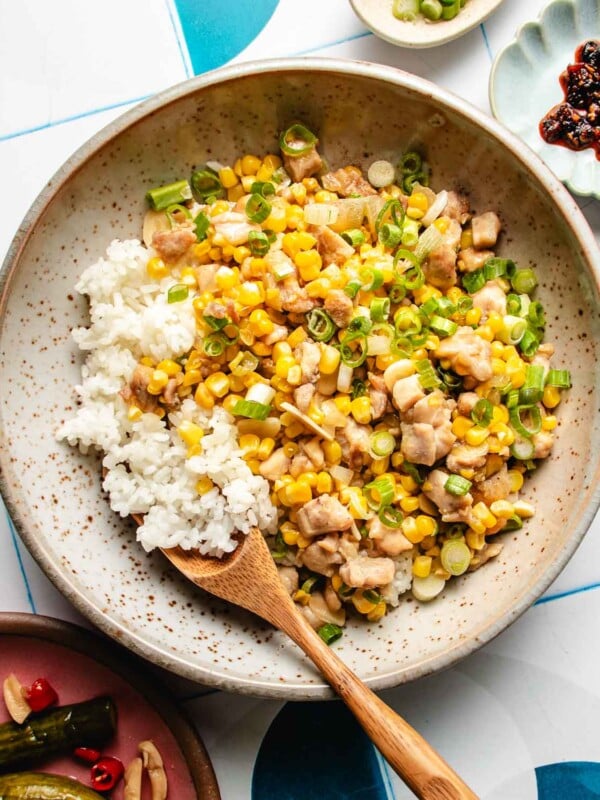 An overhead image shows a plate of sweet corn kernels sauteed with chicken and served with rice on a plate.