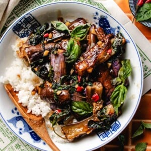 Image shows Thai basil eggplant coated with sweet basil sauce, served with rice in a blue white color bowl.