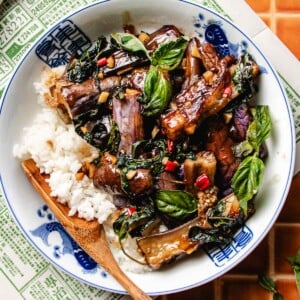 Recipe image shows Thai eggplants stir fried with fresh basil, served with rice in a bowl.